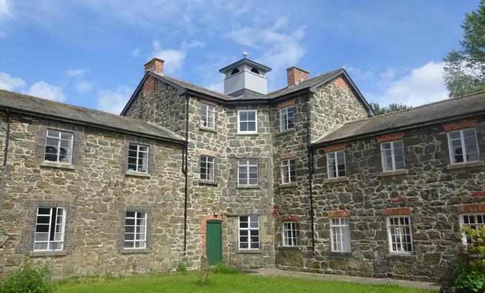A three-storey building with an octagonal core and a classical cupola, flamked by two-storey wings and built of stone.